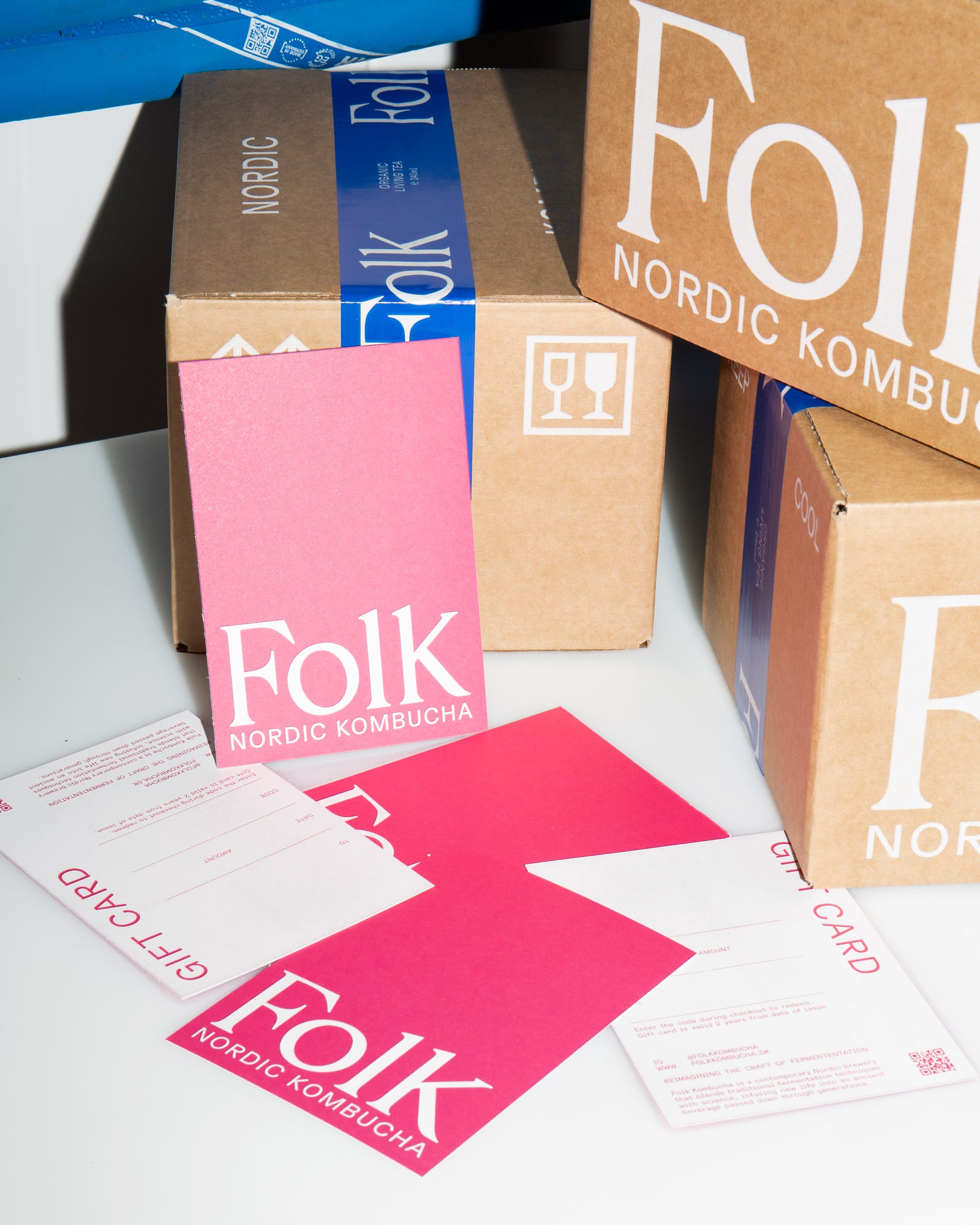 Folk Kombucha gift cards in pink beside shipping boxes with the Folk Nordic Kombucha logo